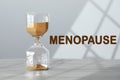 Menopause word and hourglass on table against light background