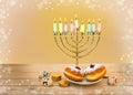 Menorah with candles, donuts, golden chocolate coins and wooden dreidels with red, blue, black letters on wooden table on light Royalty Free Stock Photo