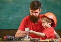 Mens work concept. Father with beard teaching little son to use tools in classroom, chalkboard on background. Boy, child