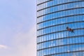 Mens workers in red and dark work clothes cleaning the exterior windows of a business skyscraper - industrial alpinism