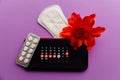 Menstruation app calendar in smartphone with sanitary pad, pills and red flower on a lilac background. Woman critical