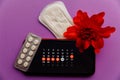 Menstruation app in smartphone with sanitary pad, pills and red flower on a lilac background. Woman critical days and