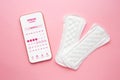 Menstruation calendar application on a smartphone lies isolated on a pink background with two women pads
