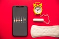 Menstruation calendar in smartphone with cotton tampon, sanitary pad and yellow alarm clock on red background. Woman Royalty Free Stock Photo