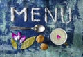 Menu with spoon, cup of milk walnuts, leaves and purple petals isolated on rugged background Royalty Free Stock Photo