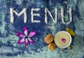Menu text made of salt with cup of milk, walnuts, bay leaves and petals  on blue rugged background Royalty Free Stock Photo