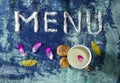 Menu text made of salt with cup of milk, walnuts, bay leaves and petals  on blue rugged background Royalty Free Stock Photo