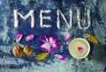 Menu text made of salt with cup of milk, walnuts, bay leaves and petals  on blue rugged background Royalty Free Stock Photo