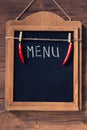 Menu written with chalk on aged blackboard with chilli peppers hanging on wooden wall Royalty Free Stock Photo