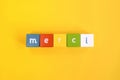 Merci - word made from colored wooden blocks. Painted cubes with letters on yellow background. Conceptual photo. Top view.