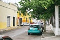 Merida / Yucatan, Mexico - June 1, 2015: The green cars parking on the stree of city of Merida with the colorful yellow building i Royalty Free Stock Photo