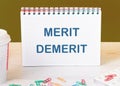 Merit, demerit and its retributions at the level of the individual. MERIT DEMERIT words in a checkered notebook on the table