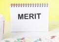 Merit the word is written on a blank sheet in a notebook standing on a table on a yellow background