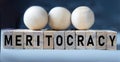 MERITOCRACY - word on wooden cubes on a blue background with wooden round balls