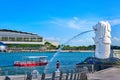 Merlion, symbol of Singapore, on Marina Bay shore. Tourist boat pass by, couple of unrecognizable adults take pictures