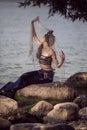 Mermaid Lady Caught In Net At Sea Coast on Rocks Wearing Seashell Decorated Crown and Black Shiny Tail On Body Covered With