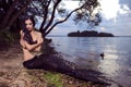 Mermaid Posing With Net Near Sea on Rocks While Wearing Artistic Makeup and Black Shiny Tail Covered With Colorful Spangles Posing