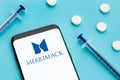 Merrimack logotype on Smart phone screen and pills and syringe on blue background