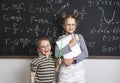 Merry boy and girl pupils are standing at the blackboard and the stetrads. Many formulas are written on the blackboard.