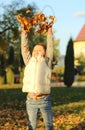 A merry child scatters an armful of yellow fallen leaves. Sunny sunset in autumn park outdoors