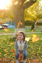 A merry child scatters an armful of yellow fallen leaves. Sunny sunset in autumn park outdoors