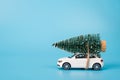 Merry Christamas concept. Side profile close up photo of mini toy white stylish modern car carrying fir tree in snow on the top of