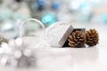 Merry christmas background, silver gift present box with bow and ribbon, next to blue Christmas balls and pine cones, useful as a Royalty Free Stock Photo