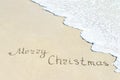 Merry Christmas caption at wet beach sand with sea wave Royalty Free Stock Photo