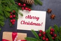 Merry Christmas card with paper, gift box, holly berries and fir tree branch on stone background. Top view Royalty Free Stock Photo