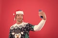 merry christmas. cheerful unshaven man in santa hat and sweater making selfie on phone. man celebrate xmas party. winter