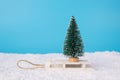 Merry Christmas concept. Closeup photo of small toy christmas tree standing on wooden retro sledges in snow and blue bright sky
