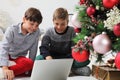 Merry christmas and coronavirus holidays, children look at the computer near the christmas tree, stay at home and christmas Royalty Free Stock Photo