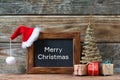 Merry Christmas decorations, chalkboard with text Merry Christmas and a red Santa hat, small Christmas tree and gifts Royalty Free Stock Photo