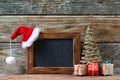 Merry Christmas decorations, empty chalkboard with a red Santa hat, small Christmas tree and gifts on a timber background Royalty Free Stock Photo