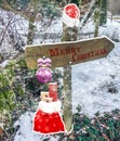 Merry christmas on a direction sign post decorated with a santa claus hat christmas ball and a bag with presents next to it all co Royalty Free Stock Photo