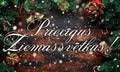 Merry Christmas displayed on a rustic wooden table with decoration, gifts, snow, tree branch in Latvian Royalty Free Stock Photo