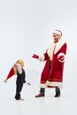 Merry Christmas. Father, man, dressed like Santa Claus having fun with little sweaty kid, sun in red hat against white