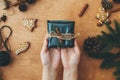 Merry Christmas, flat lay. Hands holding stylish rustic christmas gift and pine branches, cones, gingerbread cookies,thread, Royalty Free Stock Photo