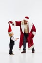 Merry Christmas. Funny father, man, dressed like Santa Claus have fun with little sweaty kid, sun against white studio