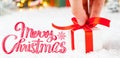 Merry Christmas greeting card with a man hand holding a gift box with red ribbon on the snow and blurred lights on the Royalty Free Stock Photo