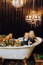 Merry Christmas and Happy Holidays! Cheerful girl and boy in a bath with Christmas gifts in gold wrappers. Royalty Free Stock Photo