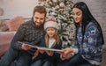 Merry Christmas and Happy Holidays Cheerful mom, dad and her cute daughter girl reading a book. Parent and little child Royalty Free Stock Photo