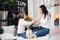 Merry Christmas and Happy Holidays. Cheerful mom and her cute daughter girl opening a Christmas present. Parent and Royalty Free Stock Photo