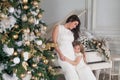 Merry Christmas Happy Holidays. Cheerful mother and her cute daughter girl with a white piano and decorated Christmas tree with