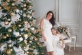Merry Christmas Happy Holidays. Cheerful mother and her cute daughter girl with a white piano and decorated Christmas tree with