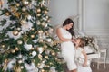 Merry Christmas Happy Holidays. Cheerful mother and her cute daughter girl with a white piano and decorated Christmas tree with