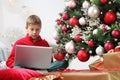 Merry christmas and happy holidays, child stay at home with computer near the illuminated and decorated tree and wrapped gift