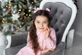 Merry Christmas, happy holidays! Cute girl with bows on head sitting on sofa against Christmas tree. child is waiting for New Year Royalty Free Stock Photo