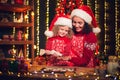 Merry Christmas and Happy Holidays. Cheerful cute curly little girl and her older sister in santas hats cooking Royalty Free Stock Photo