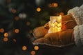 Merry Christmas and Happy Holidays! Hands in gloves holding little glowing house on background of illuminated christmas tree Royalty Free Stock Photo